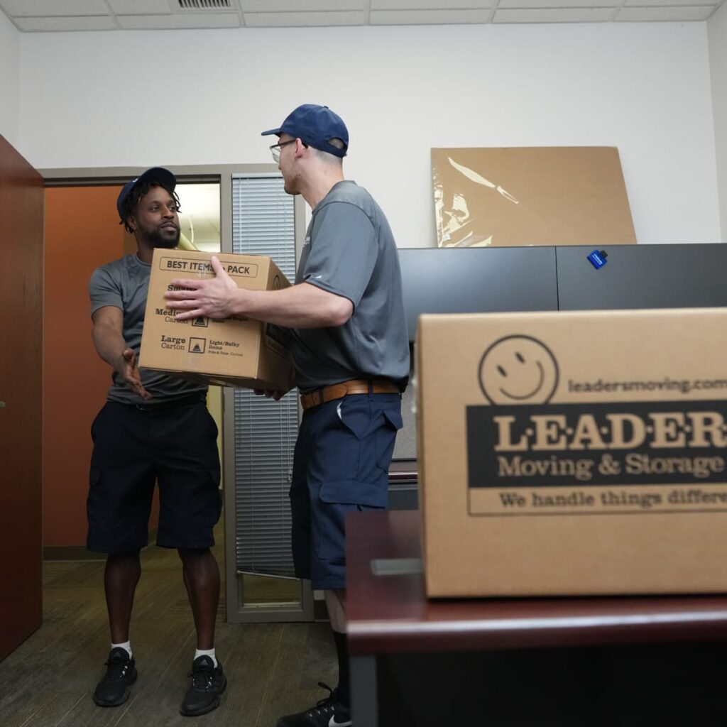 One Leaders Moving & Storage Co. team member passes a box to another in an office unit during a staging