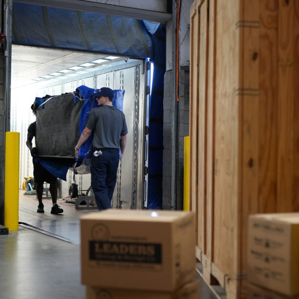 Two Leaders Moving & Storage Co. team members work together to carefully load a large item into a truck