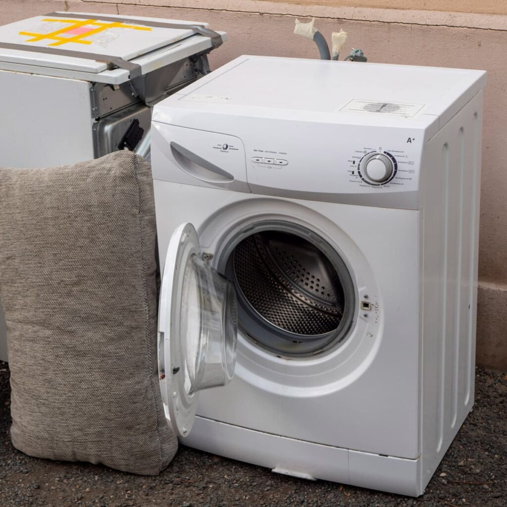 An old and broken washing machine and clothes dryer sit next to a pillow