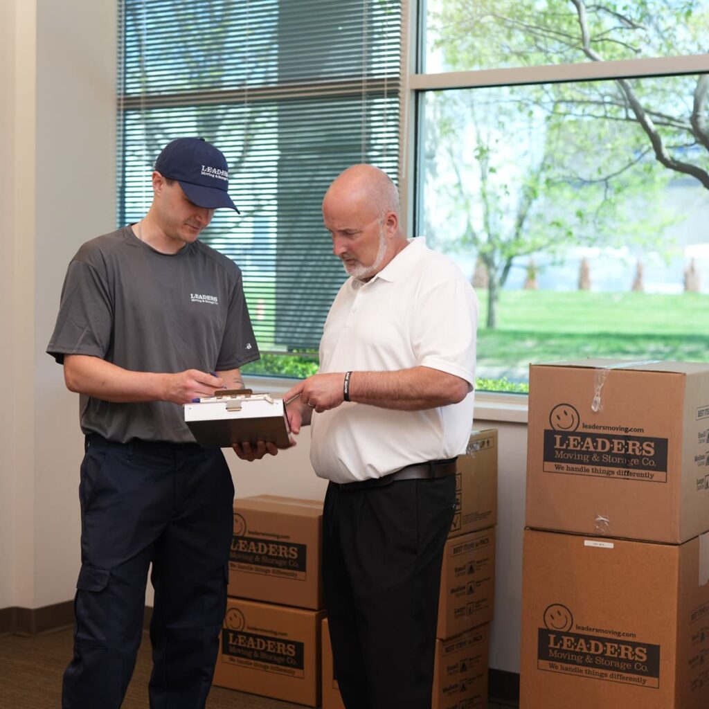 A Leaders Moving & Storage Co. moving team member stands with and meets with a business owner during an office move