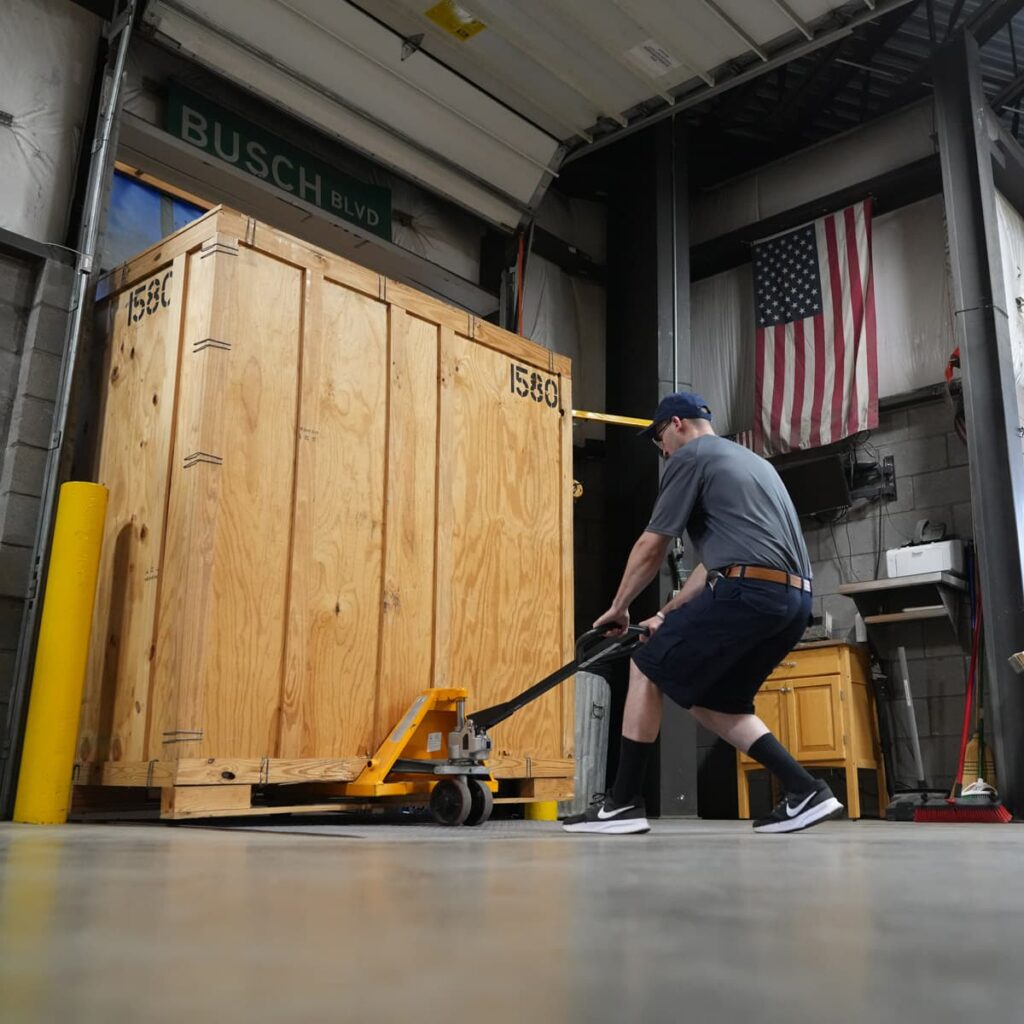 A Leaders Moving & Storage Co. team member carefully unloads a large wooden crate from a truck parked in a loading dock bay