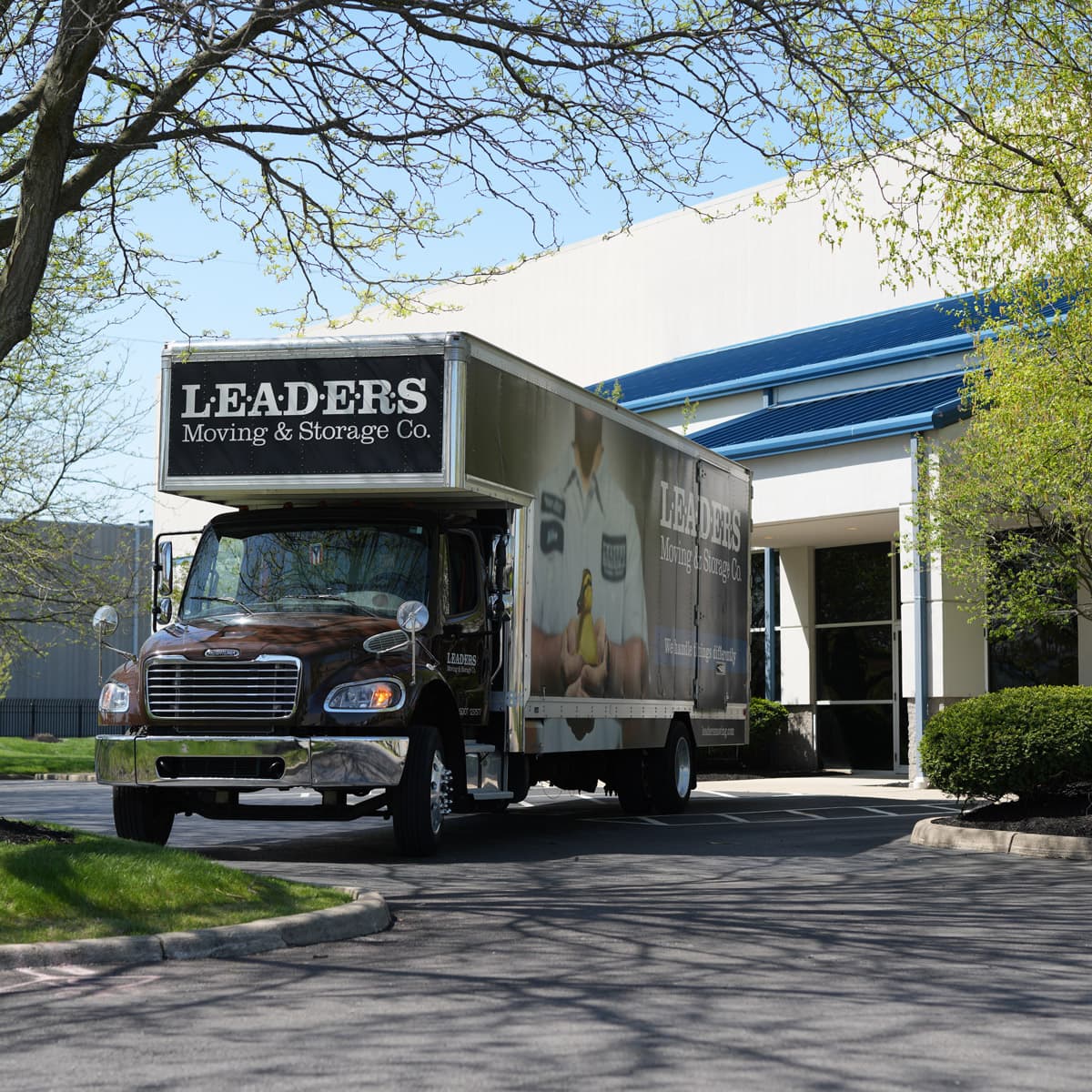 A Leaders Moving & Storage Co. truck parked in front of a Leaders facility on a sunny day